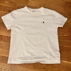 Vit t-shirt Polo Ralph Lauren - Klassisk vit t-shirt från Polo Ralph Lauren med liten broderad logga på bröstet. T-shirten är i mjuk bomull och har en enkel, rak passform med korta ärmar och rund hals. Perfekt för en clean och stilren look.