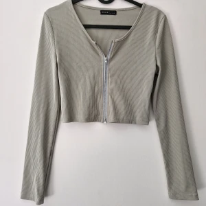 Grön croppad ribbad ziptröja från Shein - Trendig grön croppad topp från Shein med långa ärmar och dragkedja framtill. Tillverkad i ribbad polyesterblandning som ger en snygg och bekväm passform. Perfekt för att skapa en stilren och modern look.