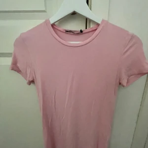 Ljusrosa basic t-shirt - Enkel och stilren ljusrosa t-shirt med rund halsringning och korta ärmar. Perfekt för en avslappnad look och lätt att matcha med jeans eller kjol. Mjuk och skön känsla i materialet.