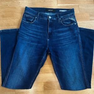 Mörkblå jeansbyxor från Replay - Säljer ett par snygga mörkblå jeans från Replay med klassisk femficksdesign och diskreta slitningar. Byxorna har raka ben och normal passform, perfekt för en stilren vardagslook. Märkeslogga på bakfickan och knappgylf.