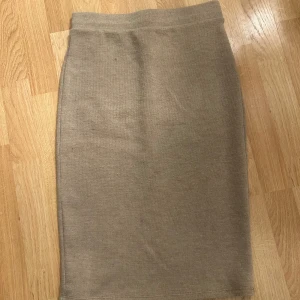 Beige stickad kjol från Vila - En beige stickad kjol från Vila i rak modell. Kjolen är midilång och har en enkel, stilren design utan detaljer eller mönster. Perfekt att matcha med en oversized tröja eller en tight topp för en chill look.🩷