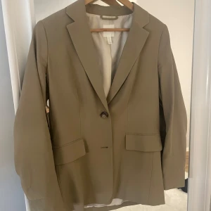 Beige kavaj från H&M med knappar - Stilren beige kavaj från H&M med klassisk krage och två knappar framtill. Super fin 😊