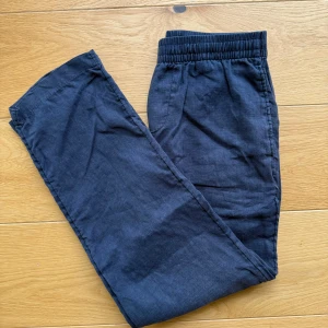 Marinblå  linnebyxor  - Snygga mörkblå linnebyxor med avslappnad passform och elastisk midja. Byxorna har raka ben, sidfickor och en bakficka. Perfekta för en chill och stilren look under varmare dagar. Priset är självklart diskuterbart!