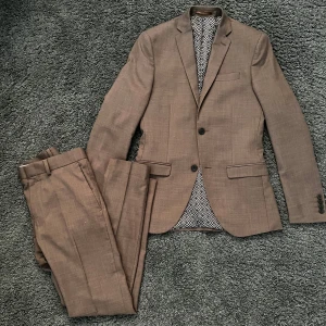 Stickad kostym  - Stilren stickad kostym i ett tunnare material, brun färg vilket gör den lite mer unik men ändå fin. Slimfit. Storlek 42, alltså cirka S 
