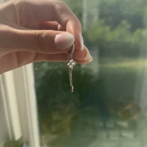 Silverfärgat örhänge med kedja och kors - Säljer ett snyggt örhänge i silverfärg med tunn kedja och ett litet kors som detalj. Örhänget har minimalistisk design och passar perfekt för dig som gillar stilrena accessoarer med en twist. 
