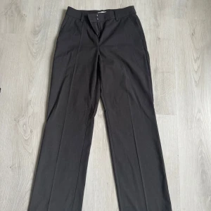 Svarta kostymbyxor från H&M - Klassiska svarta kostymbyxor från H&M med raka ben och pressveck. Byxorna har hällor för bälte, sidfickor och stängs med dragkedja och knapp. Perfekta för en clean och stilren look. Materialet är en blandning av polyester och viskos.