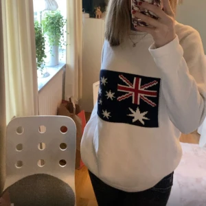 Vit sweatshirt med australiensisk flagga - Går att pruta!!!! Vit sweatshirt med stor australiensisk flagga framtill i blått, rött och vitt. Tröjan har en klassisk rund halsringning och långa ärmar. Perfekt för dig som vill sticka ut med en cool och unik look💕