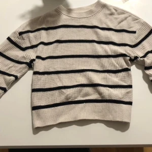 Randig stickad tröja från H&M - Säljer en stickad tröja från H&M i storlek S. Tröjan är vit med svarta horisontella ränder, har rund hals och långa ärmar. Perfekt för lager-på-lager och chill dagar. Materialet är mjukt och ger en avslappnad vibe.