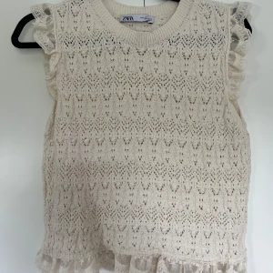 Stickad ärmlös topp med volang Zara - Supersöt stickad topp från Zara i ljusbeige med volangdetaljer. Toppen är ärmlös och har en virkad stil, den har aldrig använts och är helt ny!