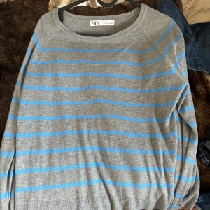 Gråblå randig tröja från Zara - Säljer en grå tröja från Zara med tunna blå ränder. Tröjan har rund halsringning och långa ärmar. Den är stickad i ett mjukt material och har en avslappnad passform som är perfekt för lager-på-lager-stil.