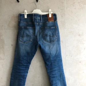 jeans från Jack & Jones - Säljer ett par blå jeans från Jack & Jones i klassisk femficksmodell. Jeansen har slitna detaljer på benen och en snygg tvättad look. De är raka i modellen och har normal passform. Perfekta för en avslappnad streetstil.