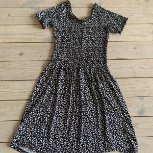 Svart blommig kortklänning UNIQ Young - Denna klänning har använts fåtal gånger. Väldigt stretchiga och skönt tyg! Supersöt svart kortklänning från UNIQ Young med vita småblommor över hela tyget. Klänningen har korta ärmar, smockad överdel och lätt utställd kjol. Perfekt för dig som gillar en feminin och bekväm stil.