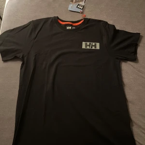 Svart t-shirt från Helly Hansen - Svart t-shirt från Helly Hansen med klassisk rund hals och diskret HH-logga på bröstet. Den är helt ny och aldrig använd. Tar bara emot Swish och kontanter, tröjan hämtas upp i Borås Hulta eller något i närheten där det passar. 