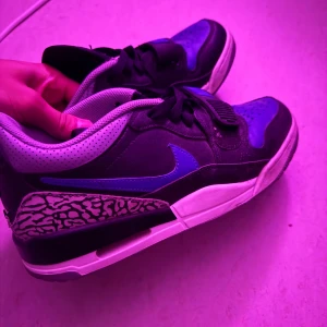 Nike sneakers med blå detaljer - Snygga Nike sneakers med svart och blå ovandel, grå perforerad vadderad häl och coolt mönstrad detalj vid hälen. Skorna har klassisk snörning, vit sula och en blå swoosh på sidan. Perfekta för dig som vill sticka ut med en unik look.