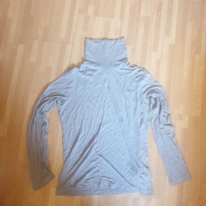 Grå polotröja från H&M Basics - En enkel och stilren grå polotröja från H&M Basics. Tröjan har lång ärm och hög polokrage, perfekt för lager-på-lager. Tillverkad i mjuk bomull som känns skön mot huden. Passar dig som gillar minimalistisk och clean stil.