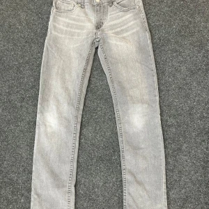 Grå Levi's 512 Slim Taper jeans - Storlek 12A.Snygga grå jeans från Levi's modell 512 Slim Taper. De har klassisk femficksdesign, smal passform med avsmalnande ben och ikonisk röd Levi's-tag på bakfickan. Perfekta för dig som gillar en modern och stilren look.