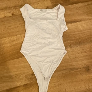 Vit ärmlös bodysuit från Zara - Säljer en vit, ärmlös bodysuit från Zara med fyrkantig urringning. Toppen är i stretchigt material och har en clean, minimalistisk look som passar perfekt till jeans eller kjol. Enkel att styla och superbekväm för alla tillfällen.