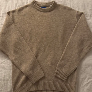 Beige stickad tröja från Jack and Jones  - Säljer en stilren beige stickad tröja från Jack & Jones. Perfekt för kyligare sommarkvällar med ribbade muddar vid ärmslut och nederkant. Passar både till jeans och chinos för en avslappnad look.  Säljer då den tyvärr är för stor för mig.  Storlek: M. Nypris: 500kr  