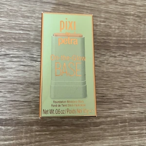 Pixi On-the-Glow BASE Nude Foundation - Helt ny, Pixi On-the-Glow BASE i färgen Nude är en foundation stick som ger en återfuktande bas. Kommer i en smidig stickform, perfekt att ta med i väskan. Förpackningen är ljusgrön med detaljer i guld och orange. Innehåller 19g.