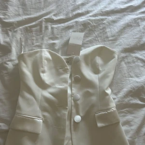Vit axelbandslös tubtopp från Zara - Stilren vit tubtopp från Zara med stora klädda knappar framtill. Aldrig använd, prislappen är på.
