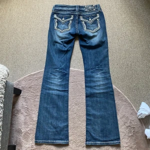 Miss Me jeans - Säljer mina favorit jeans då dom tyvärr inte passar längre😭Midja 37cm, innerben 82cm💕Snygga blå jeans från Miss Me med bootcut passform och låg midja. Jeansen har vita kontrastsömmar och broderade bakfickor med dekorativa detaljer och nitar. 💋Världens snyggaste med diamanter och mönster😍Jeansen är i en gammal modell och vintage🤩Fickorna har knappar så man kan stänga eller öppna de! Tillverkade i stretchig denim för skön passform. Storlek 26=XS, kanske liten S🙏🏻Inga fel eller defekter👑