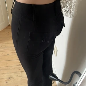 Svarta kostymbyxor från Gina Tricot XS - Säljer ett par svarta kostymbyxor från Gina Tricot i storlek XS. Byxorna är utsvängda och har snygga fickor med lock och knapp bak. Materialet känns mjukt och följsamt.