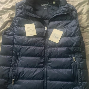Marinblå dunväst från GANT - Snygg marinblå dunväst från GANT. Säljer då jag ej använder den nåt. I väldigt bra skick som ny använd max 3-4 gånger därav som ny. Perfekt lager-på-lager-plagg för kyliga dagar. Ny priset 1500kr. Hör av vid frågor/funderingar. Priset kan diskuteras vid snabb affär👍😁