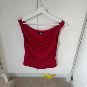 Röd draperad axelbandslös topp Bik Bok - Snygg röd axelbandslös topp från Bik Bok med draperad front och breda axelband. Perfekt för dig som vill sticka ut med en färgstark och trendig look. Toppens material är mjukt och följsamt, vilket gör den bekväm att bära.