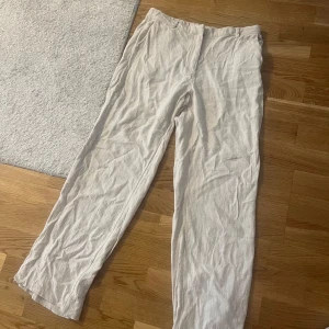 Beiga linnebyxor från Nelly, stl 40 - Snygga beiga linnebyxor från Nelly i rak modell. Byxorna har hög midja, hällor för bälte och två bakfickor. Perfekta för en chill och stilren look under varmare dagar.