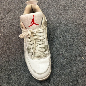 Nike Air Jordan 4 Retro Vit/Röd - Säljer ett par Nike Air Jordan 4 Retro i vitt skinn med grå detaljer och röd Jumpman-logga på plösen. Klassisk siluett med snörning, meshpaneler och stänkmönstrad grå sula. Perfekta för dig som gillar ikoniska sneakers med streetkänsla.