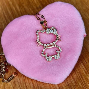 Fint guldtonat halsband  med strass & Hello Kitty-motiv! - Sött och exklusivt guldtonat halsband i rostfritt stål med Cubic Zirkonia & Hello Kitty-motiv. Kedja medföljer. Höjd berlock: 2,5 cm. Kedja: 40 cm (+5). Kommer i fin ask. Oanvänt.