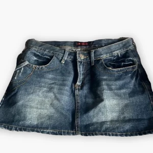 Minikjol jeanskjol från Cipo & Baxx - Snygg blå jeanskjol från Cipo & Baxx i kort modell. Klassisk femficksdesign med slitna detaljer och rå kant nertill. Perfekt för dig som gillar en avslappnad och trendig stil. Tydliga sömmar och knapp med logga framtill.