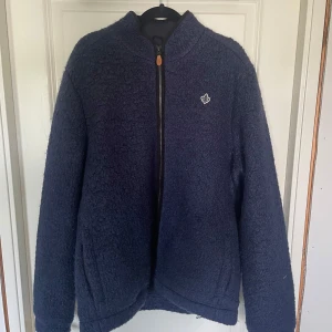 Mörkblå teddyjacka från Morris  - Säljer en mörkblå teddyjacka från Morris i storlek L. Jackan har en mysig, fluffig yta, hel dragkedja framtill och en liten broderad logga på bröstet. Helt ny och aldrig använd.                                                                                     Nypris -2699kr.                                                               Finns i ett djur och rökfritt hem.
