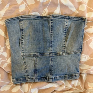 Jeans tubtopp från Zara XS - Säljer en snygg jeans tubtopp från Zara i storlek XS. Toppen är sydd i ljusblå denim med markerade sömmar och har en klassisk bandeau-form. Perfekt att styla med höga byxor eller kjol för en cool look.