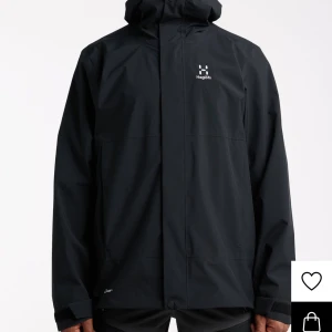 Svart regnjacka från Haglöfs - Svart regnjacka från Haglöfs med minimalistisk design och huva. Jackan har diskret logga på bröstet och justerbara ärmslut. Perfekt för blöta dagar och enkel att matcha med allt. Den är S men sitter som M