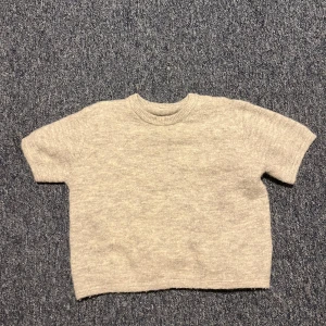 Grå stickad kortärmad tröja Gina Tricot - Supermjuk och enkel grå stickad tröja från Gina Tricot med korta ärmar och rund hals. Perfekt för lager-på-lager och chill vibes. Passar dig som gillar en clean och basic look.