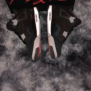 Nike Air Jordan 4 Retro SE Black/Steel Grey - Nike Air Jordan 4 Retro SE i svart och ljusgrå med vita och röda detaljer. Klassisk mesh och skinn på ovandelen, ikoniska plastdetaljer och Jumpman-logga på tungan och sulan. Snygg och tidlös siluett med snörning och platt sula.