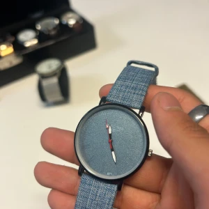 Blå Longines klocka med denimarmband - Snygg klocka från Longines med blå urtavla och matchande blått denimarmband. Boetten är rund och svart, och visarna är vita med röda detaljer. Baksidan är i rostfritt stål. Perfekt accessoar för en cool och avslappnad stil. Priset är inte hugget i sten!