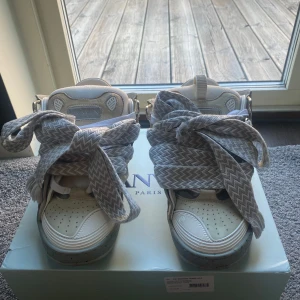 Lanvin sneakers med breda snören - Lanvin sneakers i beige och grått med breda, mönstrade snören i zickzack. Skorna har rund tå, perforerad tåbox och detaljer i mocka och skinn. Snygg kontrast mellan material och färger, samt robust sula med Lanvin-logga undertill.