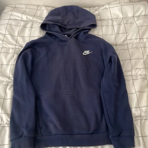 Mörkblå Nike hoodie XL - Snygg mörkblå hoodie från Nike med klassisk logga på bröstet. Tröjan har huva, känguruficka och ribbade muddar. Perfekt för chill dagar eller när du vill ha en sportig look. Mjuk insida och enkel att matcha med jeans eller joggers.