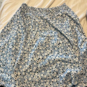 Blommig blå kortkjol från 157 - Supersöt blå kortkjol från 157 med vita och svarta små blommor. Kjolen har resår i midjan för en bekväm passform och är perfekt för varma dagar. Tunt och lätt material som känns luftigt och fräscht.