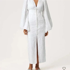 Vit adooreklänning - Superfin vit långklänning med djup v-ringning, puffiga långärmar och knappar framtill. Klänningen har broderade blommor i tyget och en slits framtill som ger en snygg touch. Perfekt för sommarens alla tillfällen! Saknar några få knappar längst ner men ingenting som syns! Nypris 1695:-🩷