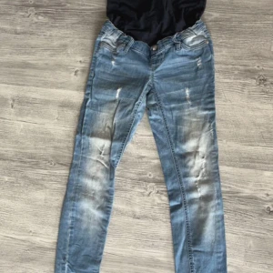 Blå gravidjeans från bpc med mudd - Snygga blå gravidjeans från bpc storlek 36 med hög svart mudd för extra komfort. Jeansen har slitna detaljer, raka ben och klassiska fickor både fram och bak. Perfekta för dig som vill ha en cool look under graviditeten.