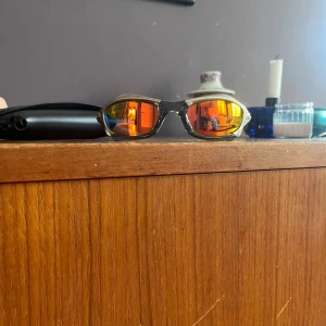 Oakley solglasögon silver/orange - Säljer ett par Oakley solglasögon med futuristisk båge i matt silver och svarta skalmar. Perfekta för dig som vill ha en sportig och unik look. Fodral ingår. Hör av er om funderingar om glasögonen eller pris!