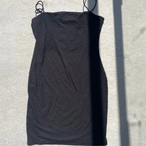 Svart ribbad kortklänning från SHEIN - Svart ribbad kortklänning från SHEIN med smala axelband och figurnära passform. Klänningen är ärmlös och har en enkel, stilren look som passar perfekt till sneakers eller klackar. Materialet är mjukt och stretchigt för en bekväm känsla.