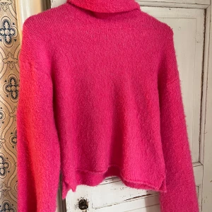 Rosa stickad polotröja - Supermjuk och fluffig rosa polotröja med långa ärmar. Tröjan är stickad och har en hög krage som ger en chill vibe. Perfekt för lager-på-lager och att mysa i under kyliga dagar.