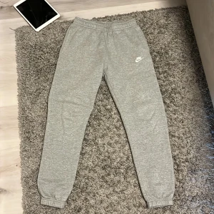 Grå mjukisbyxor från Nike - Gråa mjukisbyxor från Nike med broderad vit logga på vänster ben. Byxorna har resår i midjan och vid bensluten, samt en bakficka. Perfekta för chill eller träning, riktigt sköna och stilrena. Storlek S, bra skick 