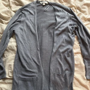 Grå lång kofta från Esprit - Mysig grå kofta från Esprit i storlek M. Lång modell med öppen front och två fickor framtill. Tunn och smidig, perfekt att slänga över en t-shirt eller topp. Långärmad och enkel design som funkar till det mesta.