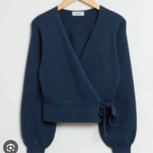 Mörkblå omlottkofta med knyt - Supersnygg mörkblå omlottkofta med knyt i sidan och v-ringad hals. Koftan har långa ärmar med bred mudd och är stickad i ett mjukt material. Perfekt att slänga över en topp för en chill men stilren look.