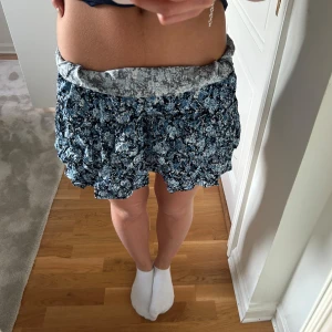 Blommig volangkjol i blått - Supersöt kort volangkjol med blått och vitt blommönster. Kjolen har flera lager och en bred, mönstrad midjeresår. Köpt i USA från Tommy Hilfiger i storlek xs för ca 600 kr. Observera att jag vikt kjolen vid midjan men går såklart att justera längd och midjehöjd.